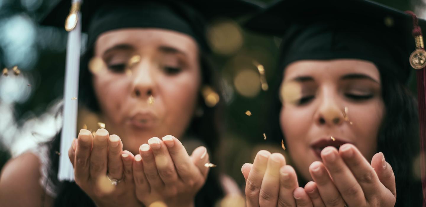 two female graduation students blowing confetti on their graduation day