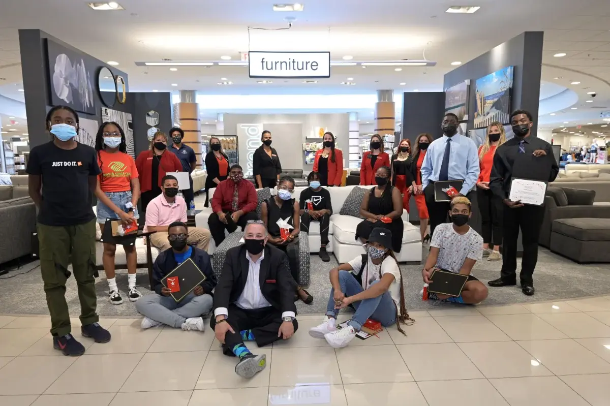 Group of people wearing masks, posing in a furniture store, some holding certificates.