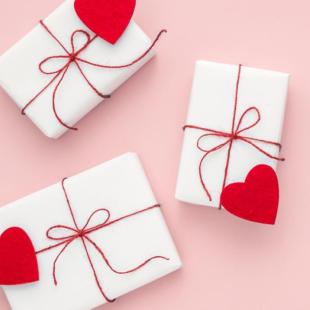 pink background with three presents wrapped in white paper with red string and heard hearts
