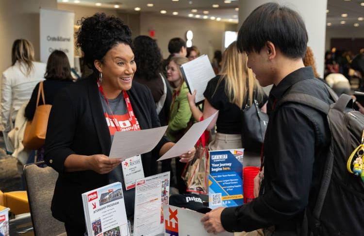 A recruiter enthusiastically greets a student looking for work during the Student Program 2025 Career Fair.